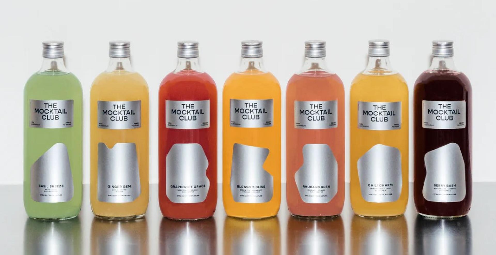 Lineup of The Mocktail Club bottled cocktails in various colors on a reflective surface