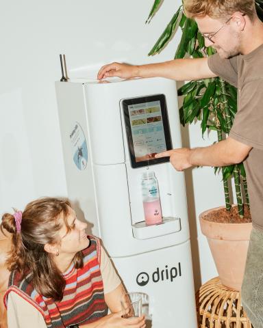 Man using a Dripl smart water dispenser while a child watches, filling a reusable bottle