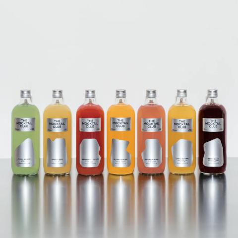 Lineup of The Mocktail Club bottled cocktails in various colors on a reflective surface