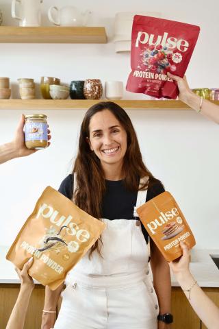 Smiling woman holding Pulse protein powders and peanut butter jar in a kitchen setting